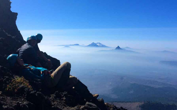 a small group of students sit high above the clouds, looking at mountain peaks in the distance
